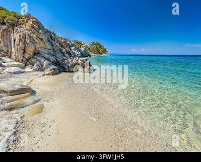 Roches plates sur le sable près d'une eau claire, plage de Fava, Sithonia, Grèce Banque D'Images