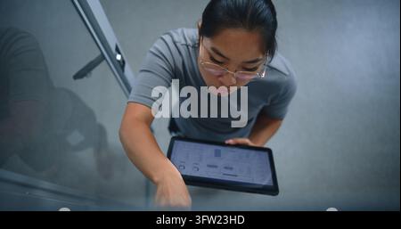 Spécialiste IT effectuant un audit physique des connexions de correctif tout en vérifiant les ports réseau par rapport aux enregistrements numériques sur une tablette. Flux de travail de salle de serveurs, infrastructure Banque D'Images