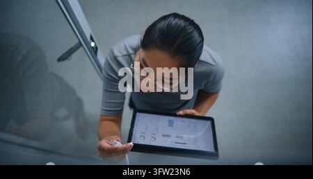 Spécialiste IT effectuant un audit physique des connexions de correctif tout en vérifiant les ports réseau par rapport aux enregistrements numériques sur une tablette. Flux de travail de salle de serveurs, infrastructure Banque D'Images