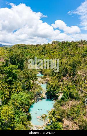 Les piscines et cascades turquoise de les chutes de Cambugahay sont entourées d'une végétation tropicale dense à Siquijor, avec de petits nageurs dans la piscine inférieure. Banque D'Images