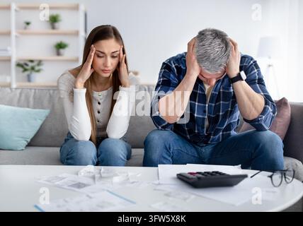 Couple mûr souffrant de difficultés avec le budget familial, ne peut pas payer les factures, a des problèmes financiers, assis avec les têtes dans les mains à la maison. Banque D'Images