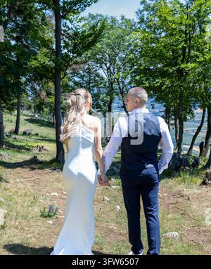 Marie et Jean marchent ensemble à travers une clairière ensoleillée de la forêt le jour de leur mariage. Banque D'Images