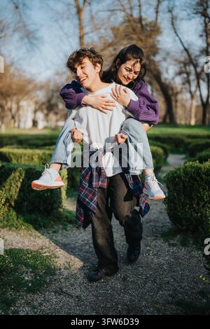 Un jeune couple profite d'un tour de pouce ludique en marchant le long d'un sentier du parc. Les deux rient et sourient alors qu'ils partagent un moment joyeux en plein air ensemble Banque D'Images