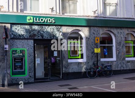 Façade de la succursale de la banque Lloyds avec un distributeur de billets vert, un revêtement en pierre, des fenêtres en arc et un vélo garé à côté de l'entrée à Newbury, Berkshire Banque D'Images