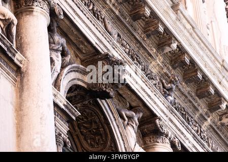 Vue architecturale rapprochée révélant des colonnes en marbre érodées sculptées avec des figures ornementales, des reliefs et des corniches superposées sur un bâtiment historique vénitien Banque D'Images