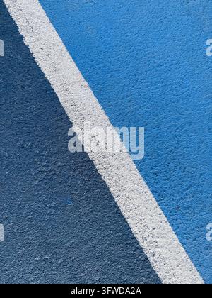 Ligne de délimitation blanche divisant une surface de terrain de sport texturée bleu clair et bleu foncé, motif géométrique abstrait en gros plan et contraste de couleurs Banque D'Images