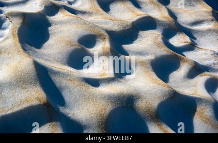 Texture de surface de neige abstraite recouverte de poussière saharienne et de pollen dans les Alpes suisses, montrant des dépôts naturels de printemps, des motifs de fonte et des sculptures Banque D'Images