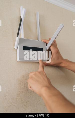 Main de personne activant un routeur sans fil mural pour établir une connexion de réseau domestique, garantissant un signal Internet fort et une connectivité maison intelligente Banque D'Images