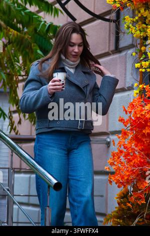Automne douillet en ville. Portrait d'une femme souriante en vêtements chauds de saison tenant une boisson chaude. Banque D'Images
