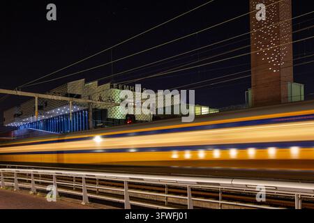 Vue d'un train à grande vitesse passant devant le bâtiment éclairé Eemhuis la nuit à Amersfoort, Utrecht, Pays-Bas. Banque D'Images