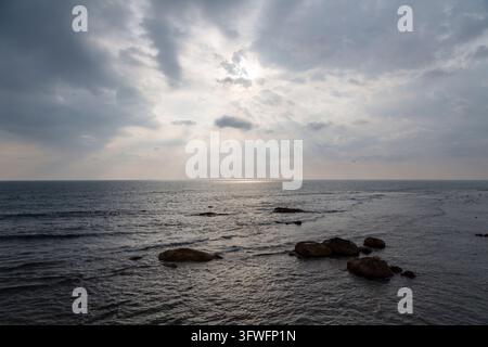 Rays de soleil à travers des nuages sombres sur une mer calme avec des rochers, Province du Sud, Galle, Sri Lanka Banque D'Images