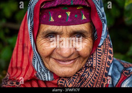 Portrait d'une femme Gujjar âgée souriante portant une casquette brodée et une écharpe rouge, Jammu et Cachemire, Naranag, Inde Banque D'Images