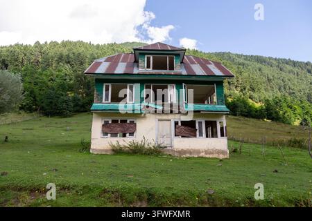 Maison abandonnée aux fenêtres brisées dans une prairie verte en contrebas d'une forêt, Jammu et Cachemire, vallée d'Aru, Inde Banque D'Images
