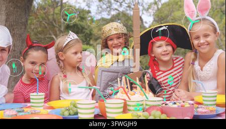 Huit enfants portant des costumes de chevalier, de pirate, de diadème et d'oreilles de lapin assis à une table de fête dans la cour Banque D'Images