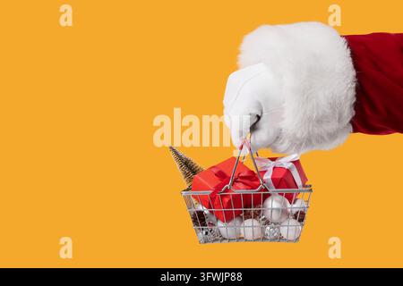 Achats de Noël et ventes au détail des fêtes, le Père Noël tenant dans sa main un panier métallique miniature rempli de boîtes cadeaux rouges et d'ornements argentés Banque D'Images