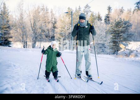 Un père aide son tout-petit à apprendre le ski de fond sur un sentier enneigé dans la région d'Helsinki, en Finlande, lors d'une sortie familiale active en hiver. Banque D'Images