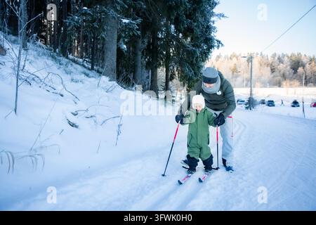 Un père aide son tout-petit à apprendre le ski de fond sur un sentier enneigé dans la région d'Helsinki, en Finlande, lors d'une sortie familiale active en hiver. Banque D'Images