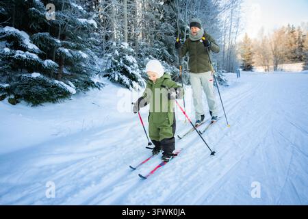 Un père aide son tout-petit à apprendre le ski de fond sur un sentier enneigé dans la région d'Helsinki, en Finlande, lors d'une sortie familiale active en hiver. Banque D'Images