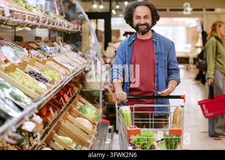 Portrait d'un homme d'âge moyen poussant un chariot de courses dans un supermarché Banque D'Images