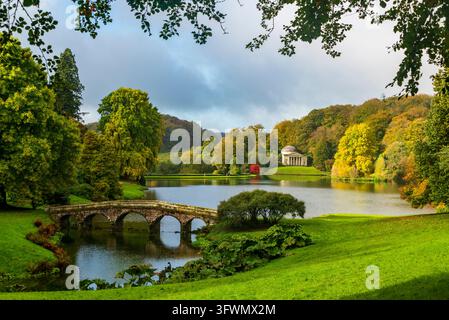 Pont en pierre en arc traversant un lac paisible avec des arbres et des pelouses colorés d'automne. Pris à Somerset et Wiltshire, en Angleterre. Banque D'Images