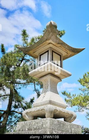 Lanterne japonaise en pierre traditionnelle avec un toit élégant de style pagode contre un ciel bleu, entourée de pins au Japon. Banque D'Images