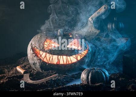Terrifiante citrouille d'Halloween sculptée, brillant en orange de l'intérieur, poignardée avec une hache, entourée d'un brouillard sombre et d'une faucille. Banque D'Images