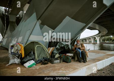 Portrait d'un homme âgé sans-abri assis près d'une tente sous un pont Banque D'Images