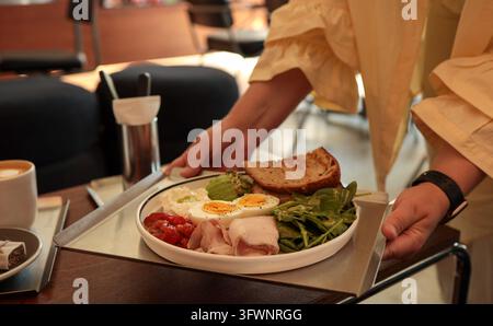 Mains féminines servant un plateau avec une assiette de petit-déjeuner sain contenant des œufs, de l'avocat et de la salade. Banque D'Images