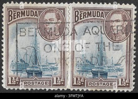 1938 Bermudes 1½d King George VI timbres-poste illustrés conservés en paire horizontale utilisée, représentant des navires et des embarcations à voile dans le port de Hamilton sous un portrait ovale du monarque britannique. Imprimés en bleu et brun, les deux timbres reliés conservent leurs perforations centrales d'origine et leurs annulations postales noires qui se chevauchent, avec des parties du cachet de la poste traversant le portrait et les scènes du front de mer. Un enregistrement distinctif de l'ère coloniale du commerce maritime des Bermudes, de l'histoire des îles de l'Atlantique, du symbolisme de l'Empire britannique et de la philatélie classique du Commonwealth. Banque D'Images