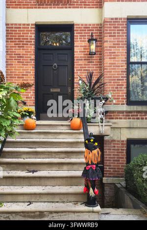 Des citrouilles, des squelettes miniatures et une décoration de sorcière bordent les marches de pierre menant à une porte d'entrée noire dans une brique rouge Banque D'Images