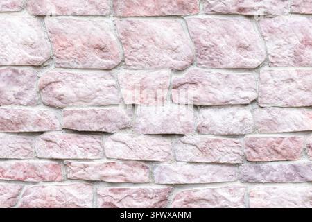 Texture de mur en pierre rose remplissant le cadre avec des blocs de pierre brute, du mortier visible et des détails de surface naturels. Les tons rose pâle et blanc cassé créent une ne Banque D'Images