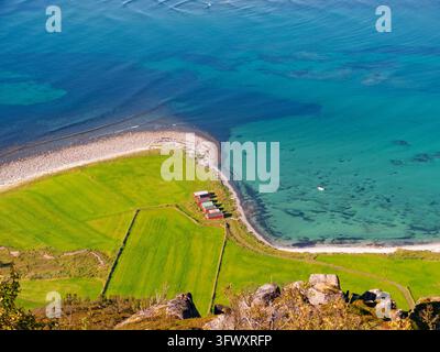 Vagan, Norvège - 20.08.2015 : Perspective aérienne de petites cabanes rouges nichées dans des prairies verdoyantes bordant une mer bleue claire et une rive de galets Banque D'Images
