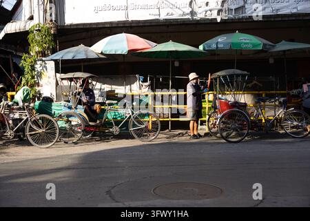 Chiang Mai, Thaïlande - 17 janvier 2026 : Des rickshaws traditionnels à vélo sont garés le long d'une route sous des parasols dans un cadre urbain. Banque D'Images