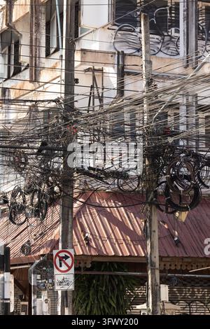 Chiang Mai, Thaïlande - 17 janvier 2026 : Un réseau chaotique de fils et câbles électriques est suspendu entre des poteaux utilitaires en béton, avec pour fond… Banque D'Images