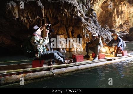 Pai, Thaïlande - 21 janvier 2026 : Trois photographes sont assis sur un radeau en bambou à l'intérieur d'une grotte illuminée à Pai, en Thaïlande. Banque D'Images