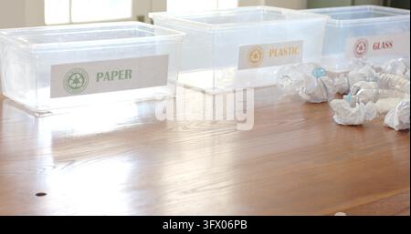 Trois bacs de recyclage transparents posés sur une table en bois près des fenêtres, montrant des étiquettes et des bouteilles Banque D'Images