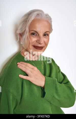 Une femme élégante d'âge moyen sourit à l'appareil, la main posée sur sa poitrine. Banque D'Images