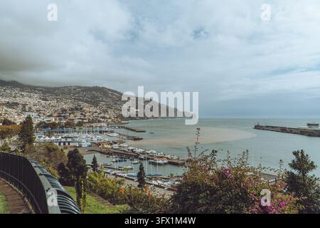 Vue panoramique du port et de la côte de Funchal à Madère, Portugal, mettant en scène des bateaux et une architecture de colline luxuriante. Banque D'Images