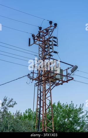 Transformateur électrique monté sur un poteau métallique rouillé contre un ciel bleu Banque D'Images