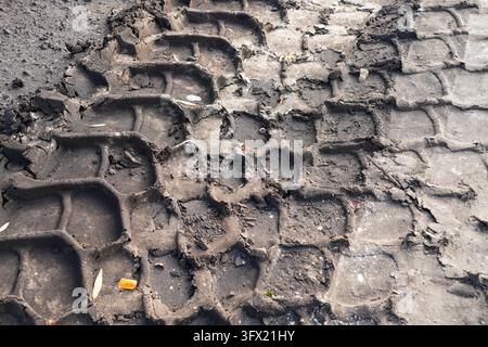 Gros plan de traces de pneus de machines lourdes profondément enfoncées dans un sol sablonneux compacté, révélant un motif de bande rugueux et une texture de sol inégale sur le chantier Banque D'Images