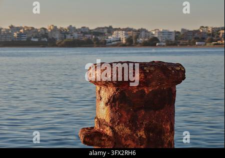 Poulie d'amarrage fortement corrodée sous un soleil chaud, avec la mer et un arrière-plan flou du front de mer, Rafina, Attique orientale, Grèce. Banque D'Images