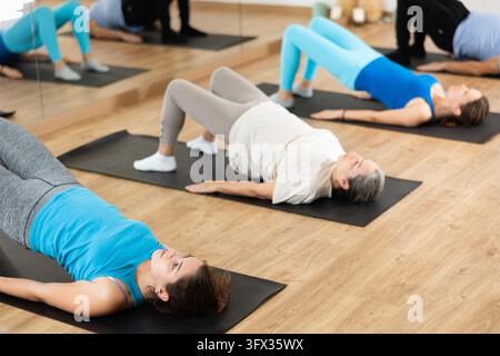 Des personnes de différents âges exécutant le pont de chute pendant l'entraînement de groupe de Pilates. Concept de bien-être et de style de vie actif Banque D'Images