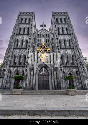 Façade de la cathédrale Saint-Joseph à Hanoï, Vietnam, comportant deux clochers jumeaux, une architecture gothique, une croix dorée proéminente et des plantes en pot sous un Banque D'Images
