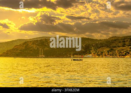 Nuages dorés dramatiques au coucher du soleil avec des rayons de lumière sur la côte du village de Sogut et les bateaux, Marmaris, Turquie Banque D'Images