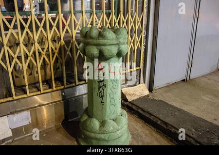 Manhattan, NYC – 24 déc. 2023 : Borne en fer vert avec des tags de graffitis devant une grille de sécurité pliante en or sur un trottoir de Chinatown la nuit. Banque D'Images