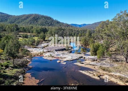 Photographie aérienne d'une rivière rocheuse sinuant entre des étagères de granit pâle et une forêt d'eucalyptus, avec des collines boisées en arrière-plan. Banque D'Images