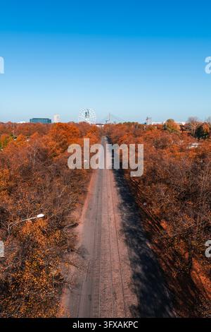 Perspective aérienne regardant vers le bas une voie de tramway droite bordée d'arbres orange d'automne menant à une grande roue et au pont suspendu de Vansu à Ri Banque D'Images
