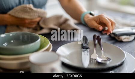 Femme met la table avec des assiettes, des bols, des couverts et une nappe Banque D'Images