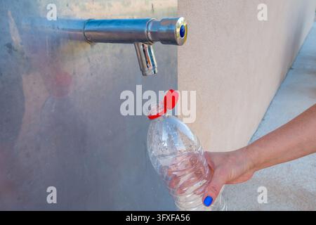 Femme remplissant une bouteille en plastique transparent à partir d'un robinet d'eau public Banque D'Images