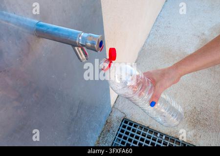 Femme remplissant une bouteille en plastique transparent à partir d'un robinet d'eau public Banque D'Images